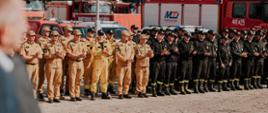 Na zdjęciu widzimy zbiórkę strażacką na zakończenie ćwiczeń ratowniczych. Na zbiórce strażacy w mundurach w kolorach piaskowym (nowe) oraz czarnym (stare).