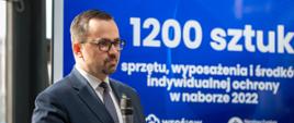 Wiceminister infrastruktury przemawia, za nim jest slajd z liczbą 1200 sztuk sprzętu. 