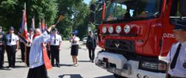 Gminny Dzień Strażaka w Dziektarzewie, na pierwszym planie ksiądz święci nowy wóz strażacki koloru czerwonego.