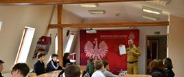 Strażak przedstawia uczestnikom konkursu arkusz z zadaniami do rozwiązania.