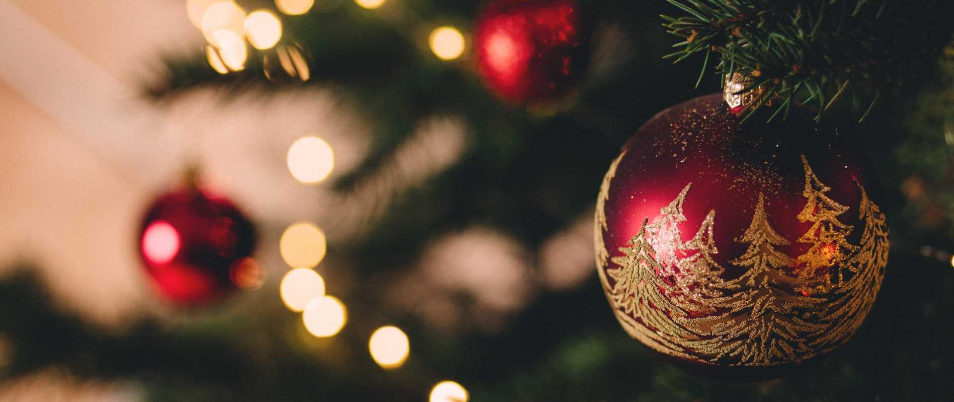 zdjęcie przedstawiające fragment choinki przystrojony w światełka oraz czerwone bombki z motywem złotych drzew iglastych