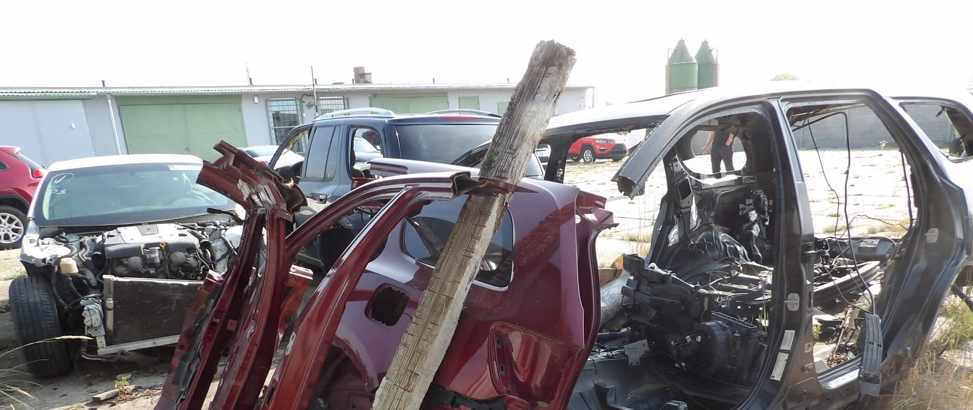 Na pierwszym planie 3 niekompletne pojazdy oraz części, całość na placu z płyt betonowych