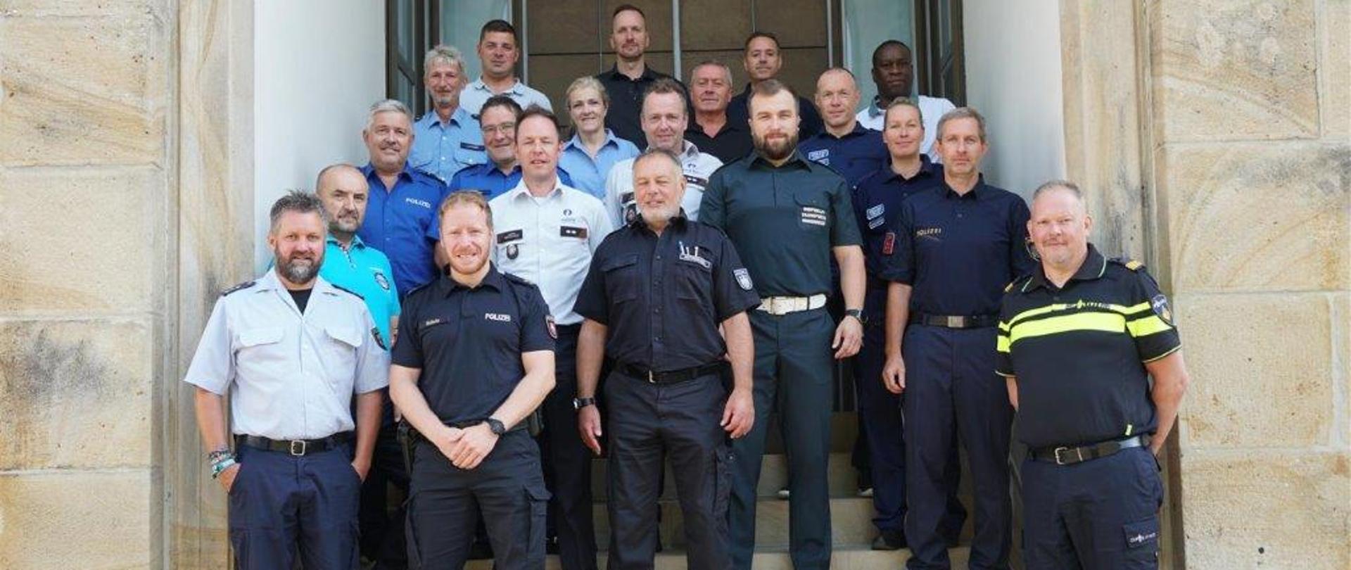 Kilkanaście osób w mundurach stoi na schodach prowadzących do budynku