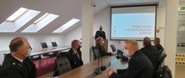 Druhowie OSP w mundurach wyjściowych w trakcie prezentacji założeń ustawy o OSP na sali konferencyjnej.