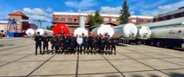 Zdjęcie grupowe uczestników szkolenia w firmie Stokota, w tle widać cysterny, uczestnicy szkolenia w szeregu, umundurowani w kaskach