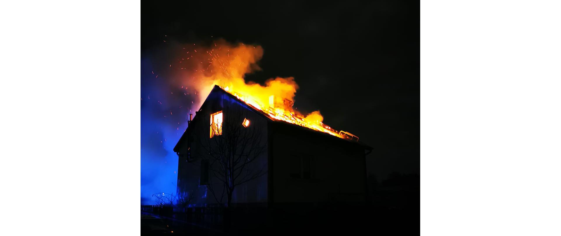 Płomieniami objęty cały dach. Płomienie wychodzą ponad dach budynku mieszkalnego. 