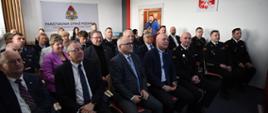 Uroczyste spotkanie w siedzibie Państwowej Straży Pożarnej w Wodzisławiu Śląskim – na pierwszym planie siedzą przedstawiciele władz i oficerowie PSP w galowych mundurach, w tle pozostali uczestnicy wydarzenia; na ścianie widoczne logo Państwowej Straży Pożarnej oraz godło Polski.