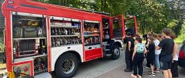 a zdjęciu widać samochód osobowy pożarniczy średni z otwartymi skrytkami podczas pokazu sprzętu harcerzom przez strażaków z JRG Skarżysko-Kamienna. W tle widać drzewa. 