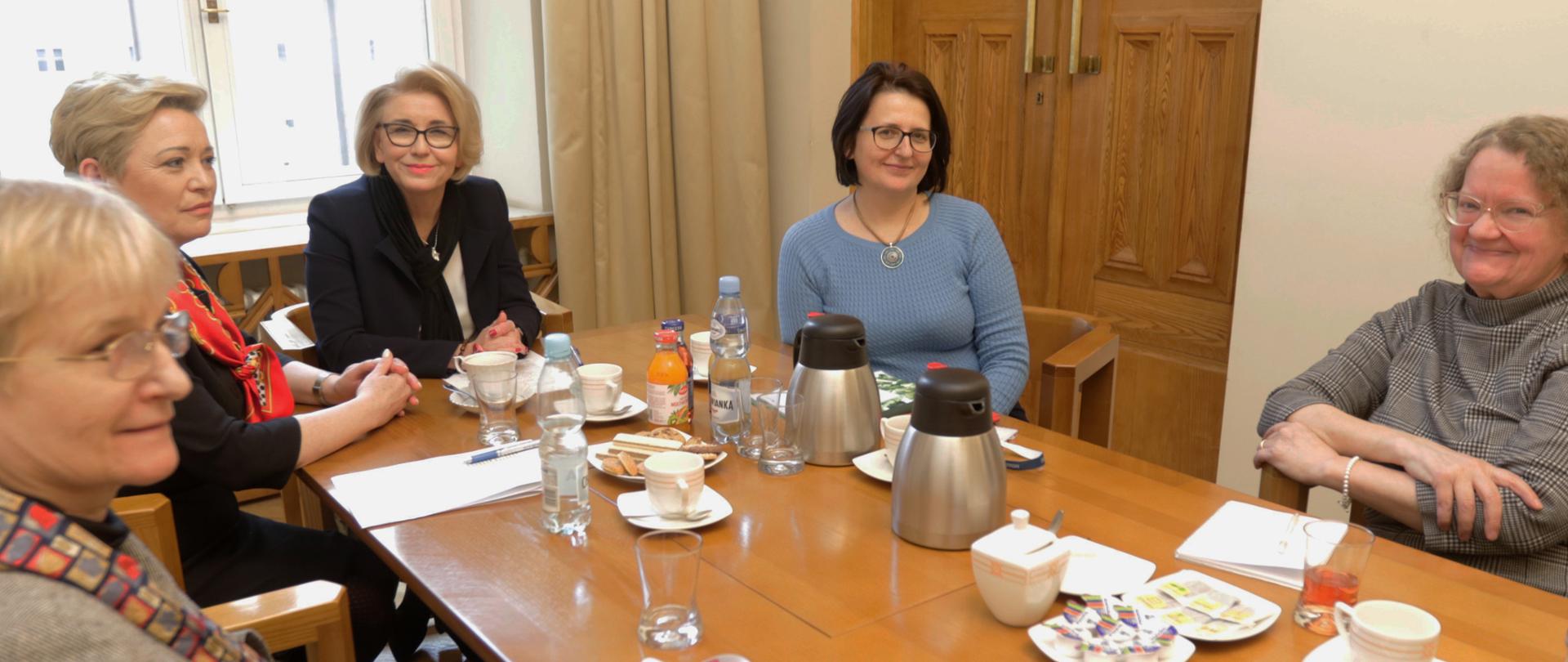 Uczestnicy spotkania z wiceminister edukacji siedzą przy stole. 