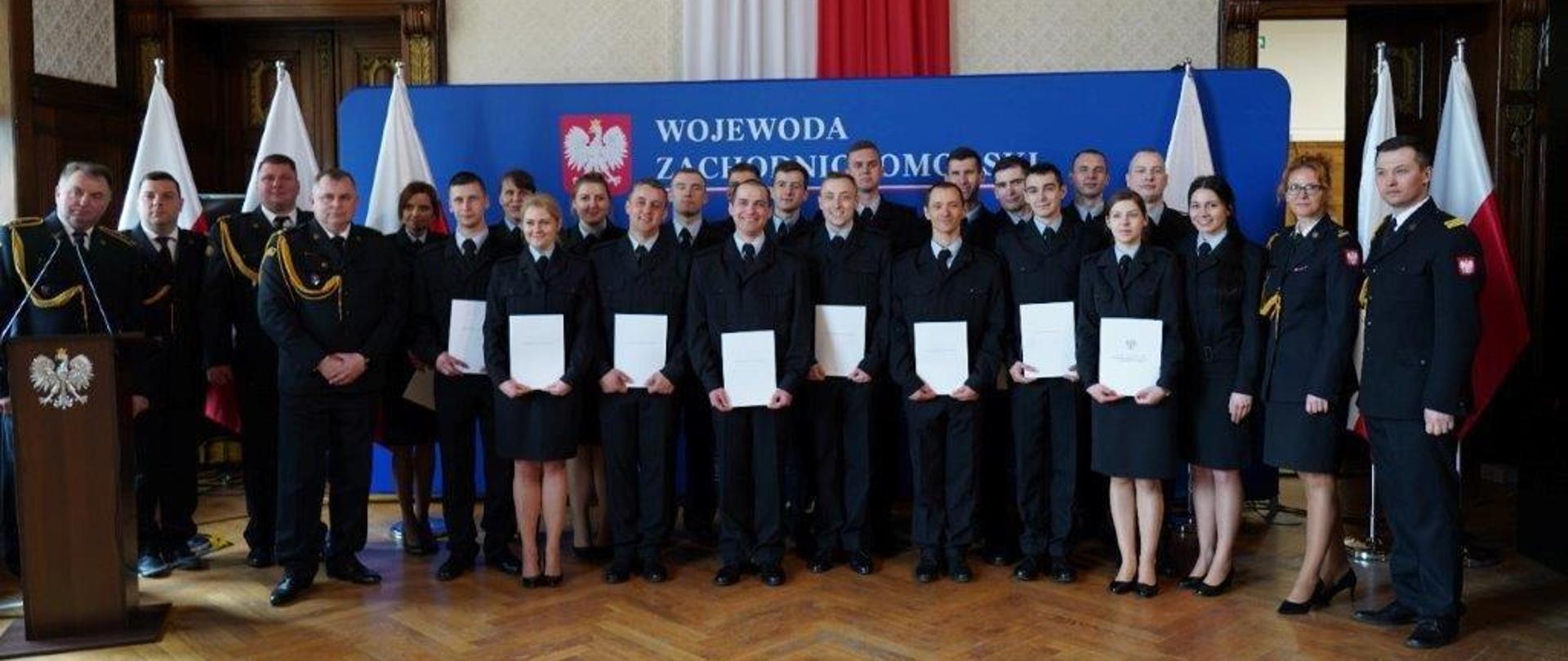 Zdjęcie przedstawia ślubujących strażaków w pomieszczeniu Zachodniopomorskiego Urzędu Wojewódzkiego w Szczecinie wraz z funkcjonariuszami Wojewódzkiego Ośrodka Szkolenia w Bornym Sulinowie