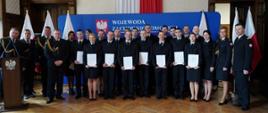 Zdjęcie przedstawia ślubujących strażaków w pomieszczeniu Zachodniopomorskiego Urzędu Wojewódzkiego w Szczecinie wraz z funkcjonariuszami Wojewódzkiego Ośrodka Szkolenia w Bornym Sulinowie