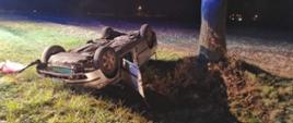 Pora nocna, samochód wypadł z drogi i przewrócił się na dach. Leży on przy drzewie. Samochód osobowy koloru srebrnego.