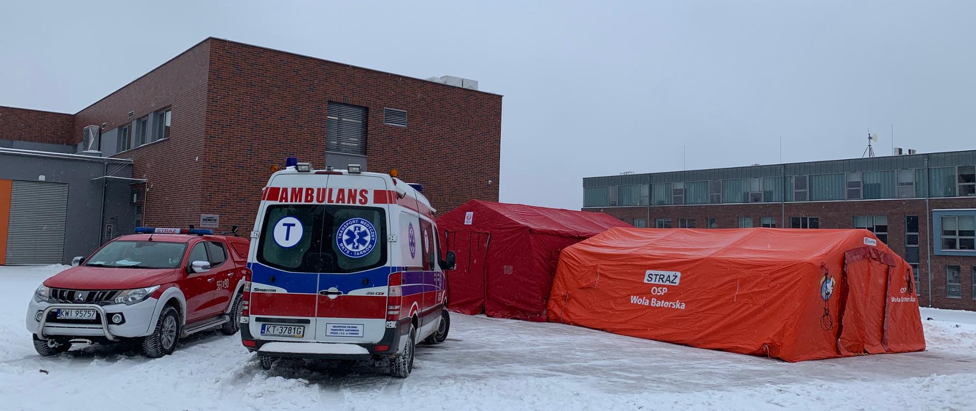 Na zdjęciu widoczne są karetka pogotowia i samochód pożarniczy. Obok znajdują się dwa namioty. Wszystko na tle budynku szkoły