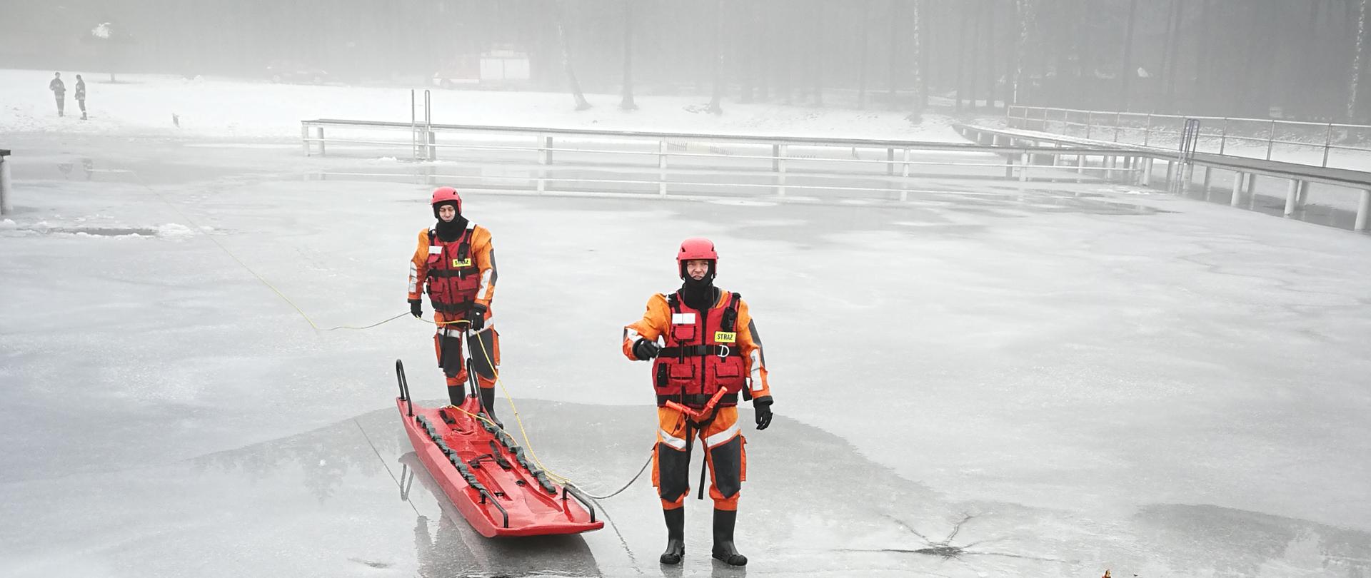 Foto przedstawia trzech strażaków podczas ćwiczeń na lodzie