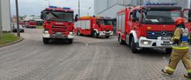 samochody pożarnicze stojące na drodze wewnętrznej. Przed nimi przechodzi dowódca akcji