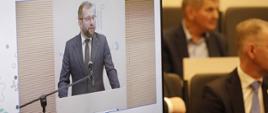 Minister funduszy i polityki regionalnej Grzegorz Puda podczas 5. Forum Akademicko-Gospodarczego, minister stoi przy mikrofonie i przemawia, na pierwszym planie widać ekran na którym jest minister Puda