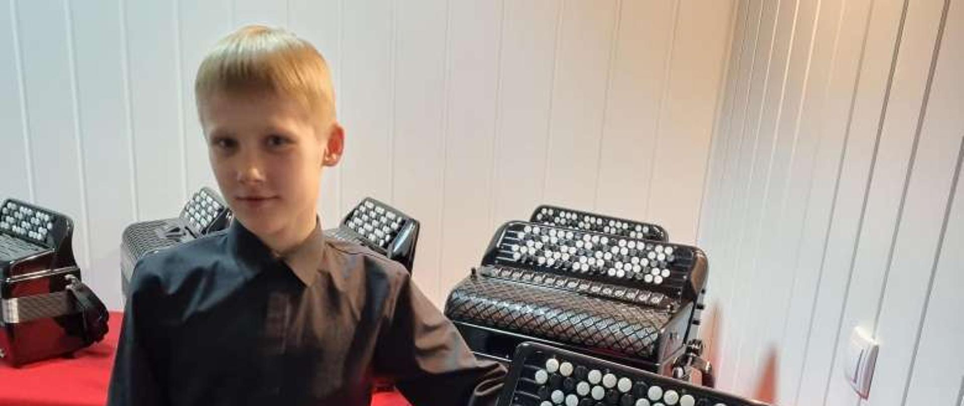 Chłopiec w czarnej koszuli, w tle wystawa akordeonów