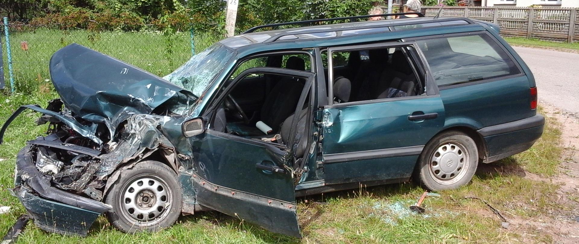 Zdjęcie przedstawia rozbity samochód osobowy koloru zielonego z uszkodzonym przodem 
