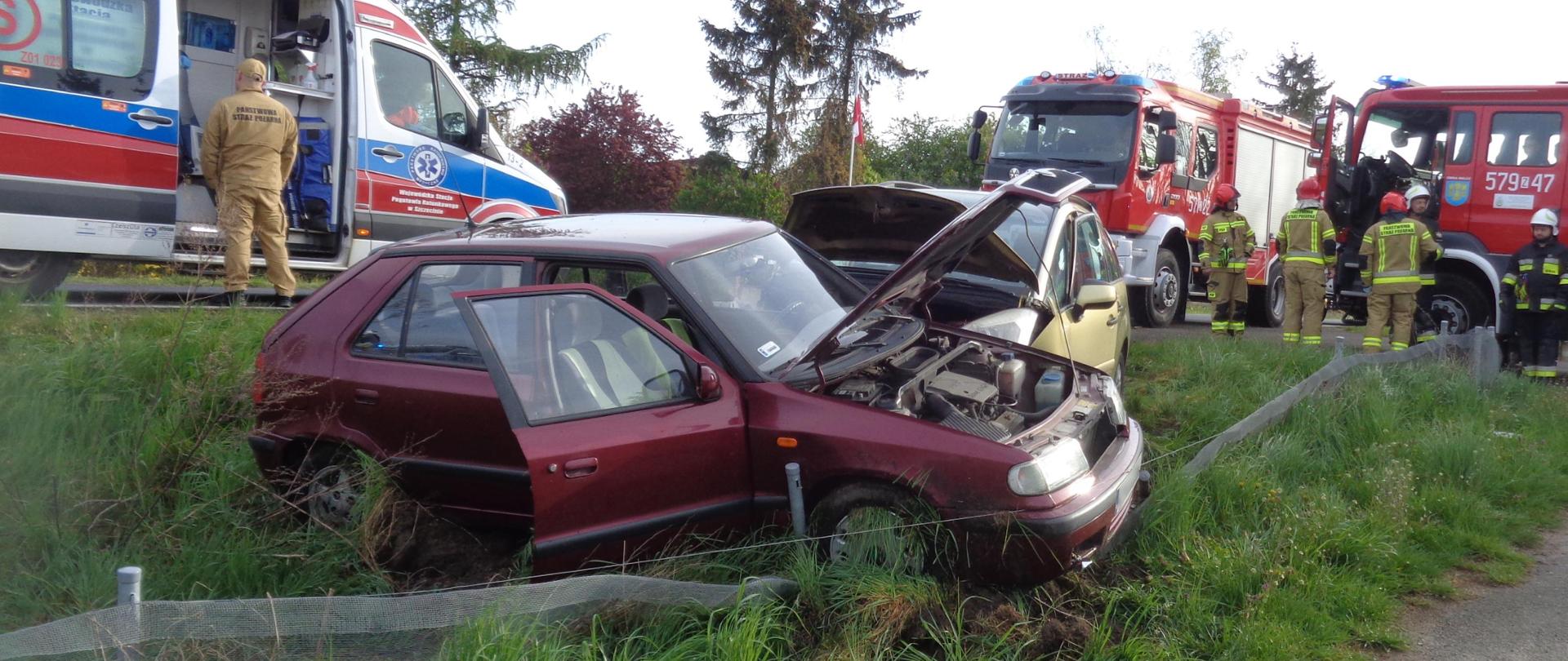 Fotografia przedstawia uszkodzony pojazd osobowy w przydrożnym rowie. W tle widać ratowników PSP i ich pojazdy oraz ZRM. 