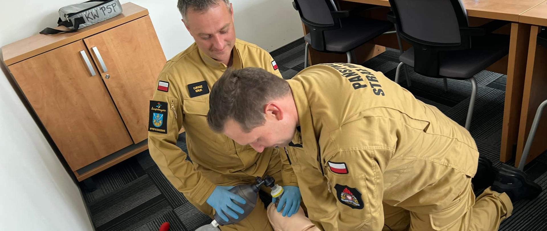 Na pierwszym zdjęciu strażacy-ratownicy wykonują symulację resuscytacji krążeniowo-oddechowej u osoby dorosłej. Jeden z ratowników wykonuje 30 uciśnięć klatki piersiowej, natomiast drugi wykonuje 2 oddechy ratownicze za pomocą worka samorozprężalnego.