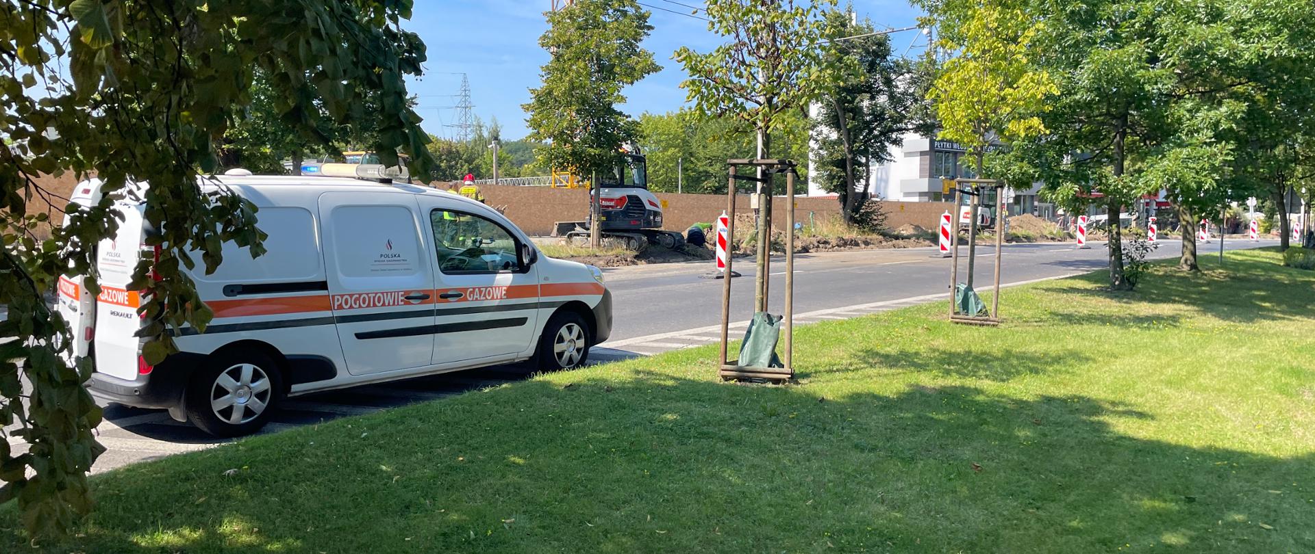 Jezdnia Alei Niepodległości przy której prowadzone są roboty drogowe. Na jezdni stoi samochód pogotowia gazowego. Na poboczu koparki oraz pracownicy pogotowia gazowego sprawdzają wyciek.