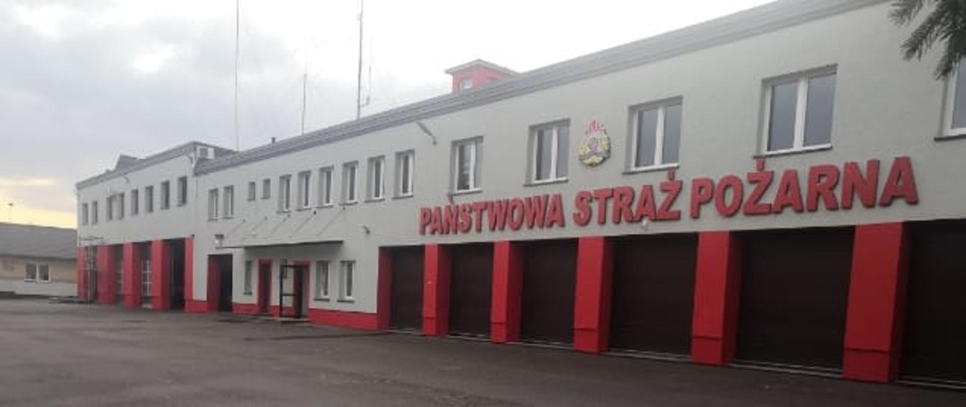 Budynek piętrowy Komendy Powiatowej Państwowej Straży Pożarnej w Makowie Mazowieckim w kolorze szarym. 11 bram garażowych jest koloru brązowego, słupy oddzielające je są czerwone. Pomiędzy garażami na środku budynku są drzwi wejściowe do komendy oraz pomieszczenia wartowni. Nad wejściem znajduje się daszek. Czerwony napis Państwowa Straż Pożarna oraz logo znajdują się nad garażami po prawej stronie. Nad budynkiem widać maszty antenowe.