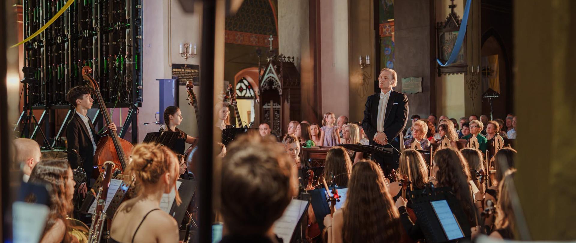 Dyrygent Ryszard Kusek prowadzi orkiestrę symfoniczną i chór PSM podczas wykonania „Missa Veni Sancte Spiritus" we wnętrzu gotyckiego kościoła parafialnego w Pilźnie, wypełnionego publicznością.