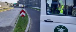 Na pierwszym planie (od prawej): przednie drzwi i prawy bok oznakowanego furgonu śląskiej Inspekcji Transportu Drogowego. Umundurowani inspektorzy prowadzą czynności służbowe z nietrzeźwym kierowcą. W tle: punkt kontrolny z rozłożonymi mobilnymi wagami inspekcyjnymi i zatrzymana za ciężka autolaweta.