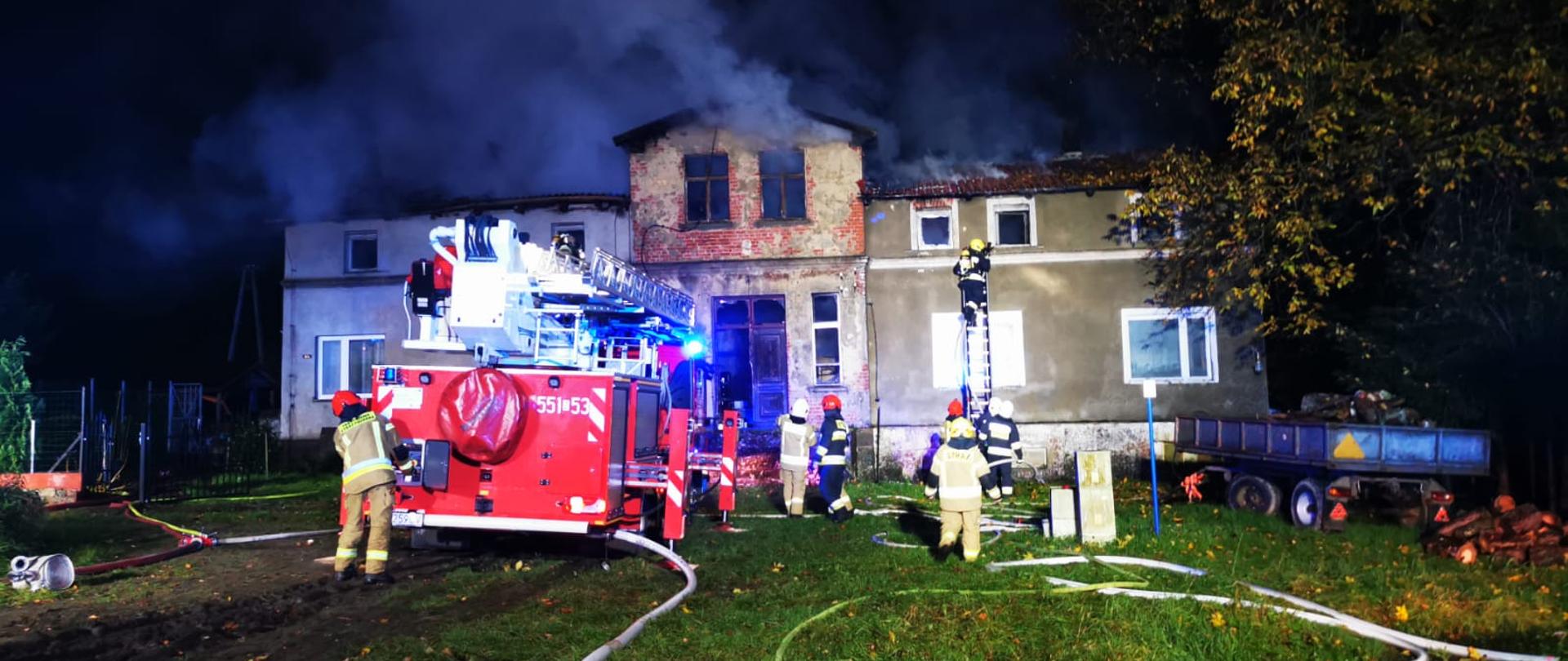 Zdjęcie przedstawia Pożar budynku wielorodzinnego w miejscowości Trzciana, strażacy gaszą go przy pomocy podnośnika.