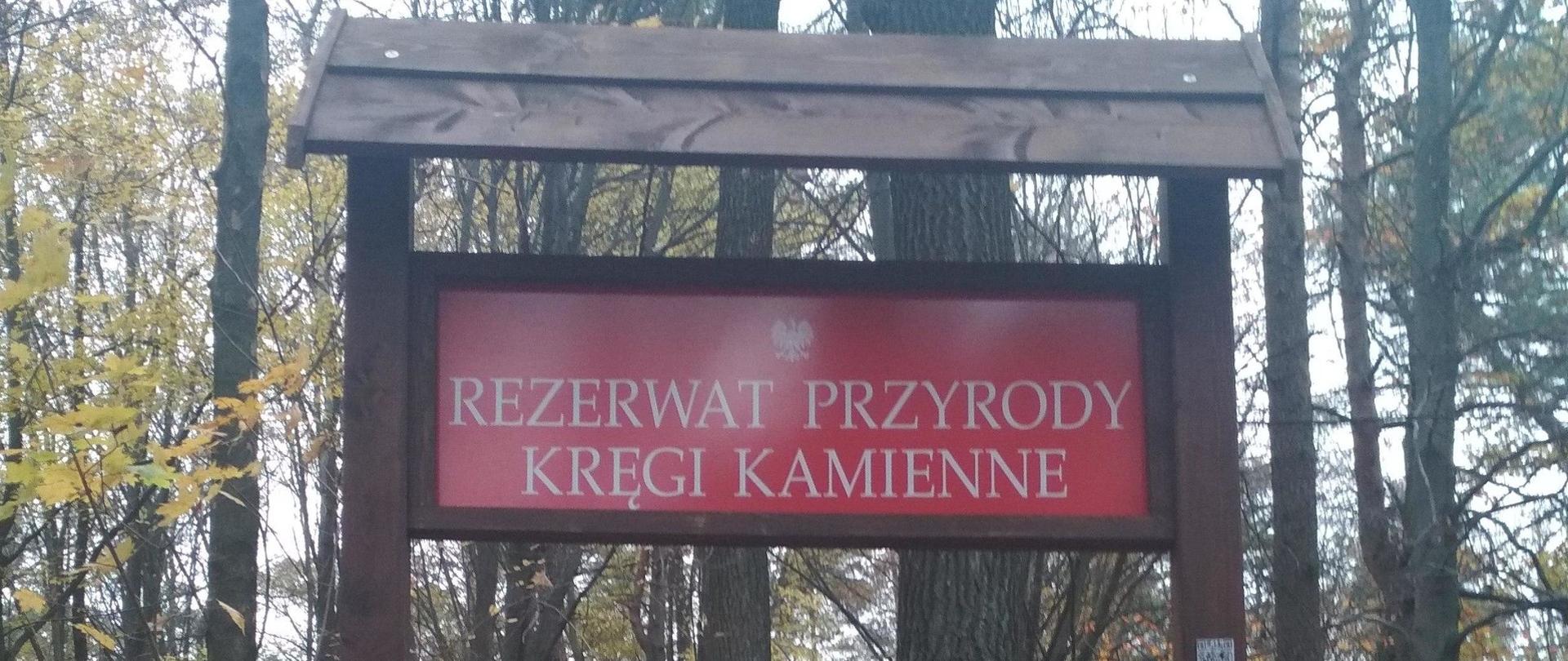 Świętokrzyskie rezerwaty przyrody: czerwona tablica informacyjna w lesie pod daszkiem z napisem Rezerwat przyrody Kręgi Kamienne