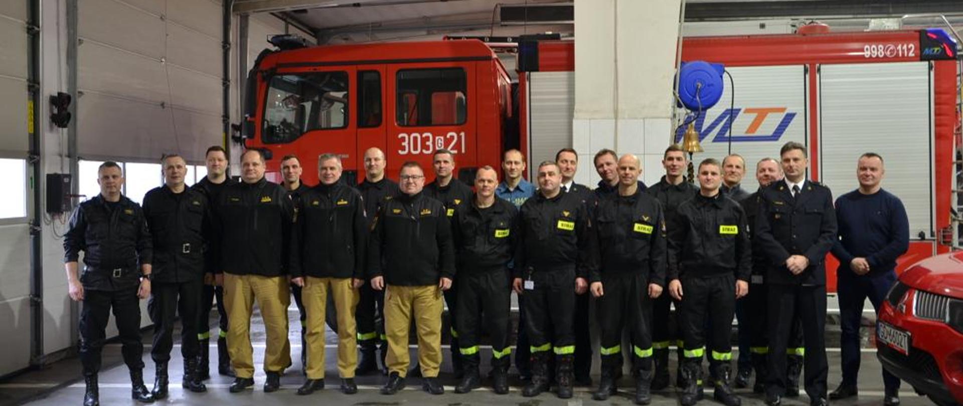 Pomorski Komendant Wojewódzki wraz z zastępcami oraz kadra KM PSP w Gdańsku i strażacy JRG 3 stoją w garażu JRG. Za plecami pojazd gaśniczy GBA.
