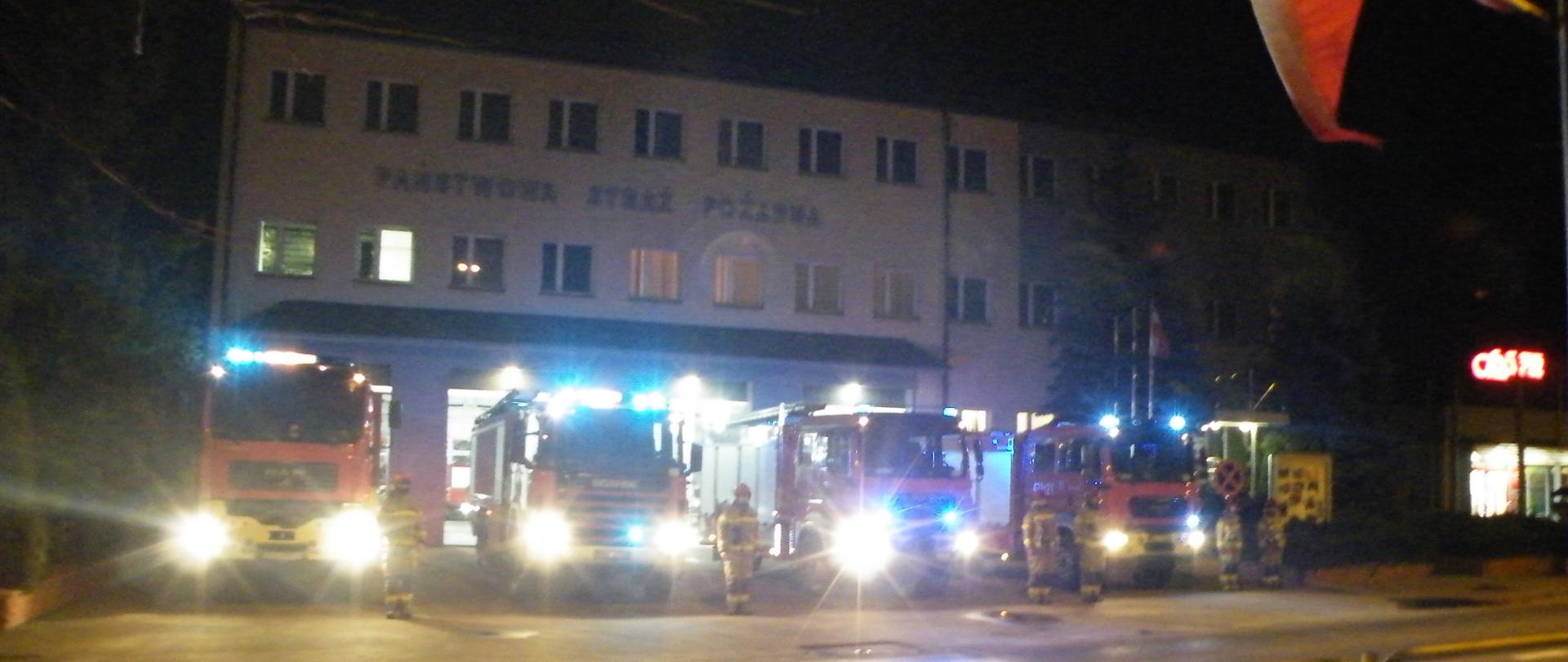 Na tle garażu samochody pożarnicze, strażacy oddają hołd zmarłym