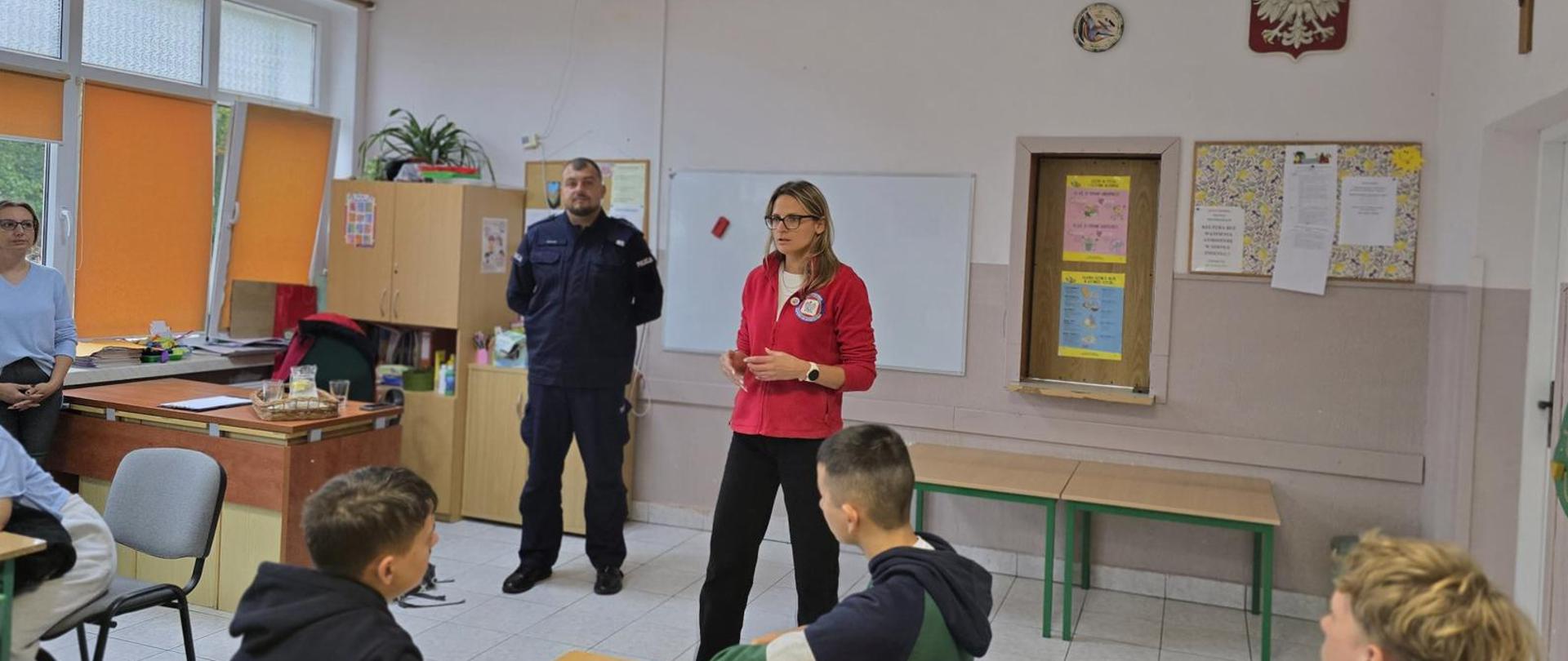 Pomieszczenie, pracownik Inspekcji Sanitarnej i Policjant stoją przed uczniami