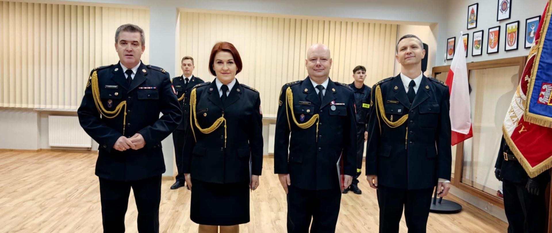 Zdjęcie przedstawia strażaków w trakcie uroczystego apelu wręczenia awansów.
W tle pomieszczenie - świetlica.
