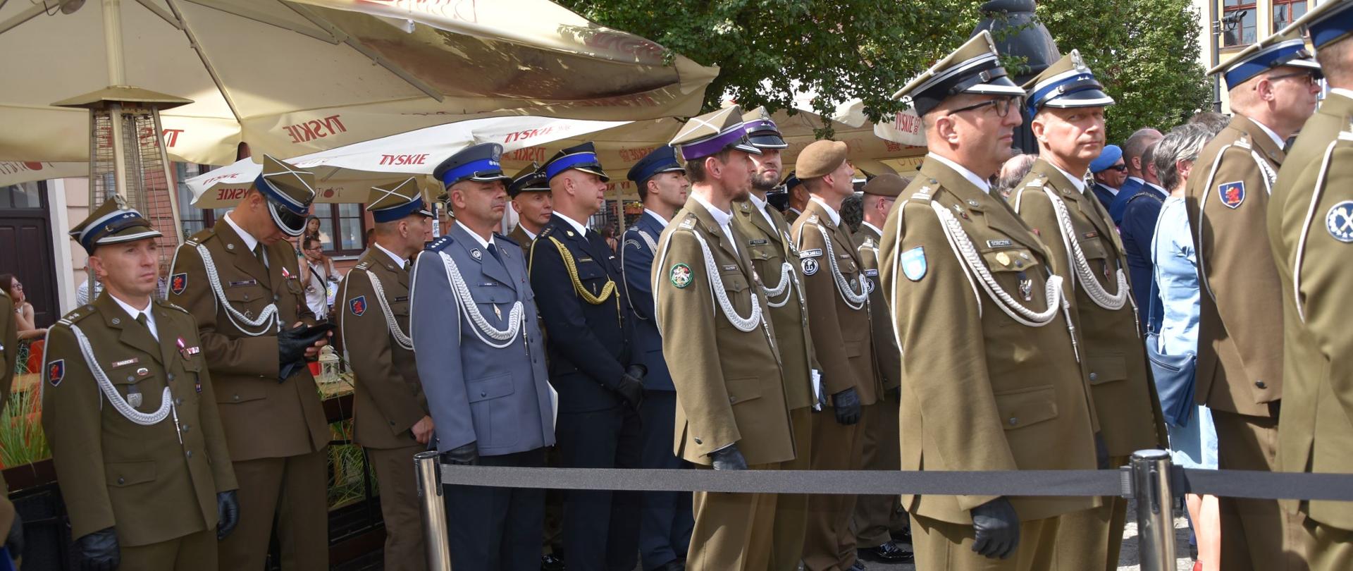 Zdjęcie przedstawia funkcjonariuszy wojska polskiego i innych służb mundurowych ubranych w mundury galowe stojących w rzędach podczas zbiórki.