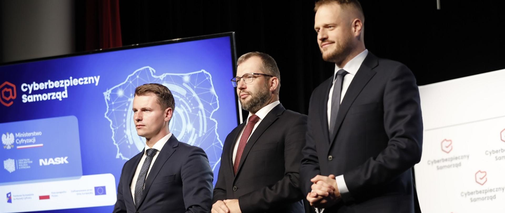 Minister funduszy i polityki regionalnej Grzegorz Puda stoi na scenie, po jego prawej stronie stoi minister cyfryzacji Janusz Cieszyński, po lewej stronie prezydent Otwocka Jarosław Margielski