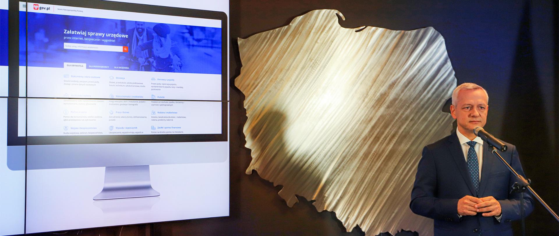 Minister Marek Zagórski stoi przed mikrofonem, w tle ekran z prezentacją strony gov.pl 