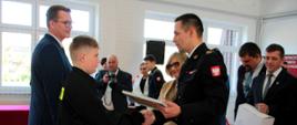 Komendant Powiatowy Państwowej Straży Pożarnej w Gorlicach wraz z zaproszonymi gośćmi wręcza podczas uroczystości dyplom uznania i upominki dla laureata szczebla krajowego w Ogólnopolskim Turnieju Wiedzy Pożarniczej „Młodzież Zapobiega Pożarom".