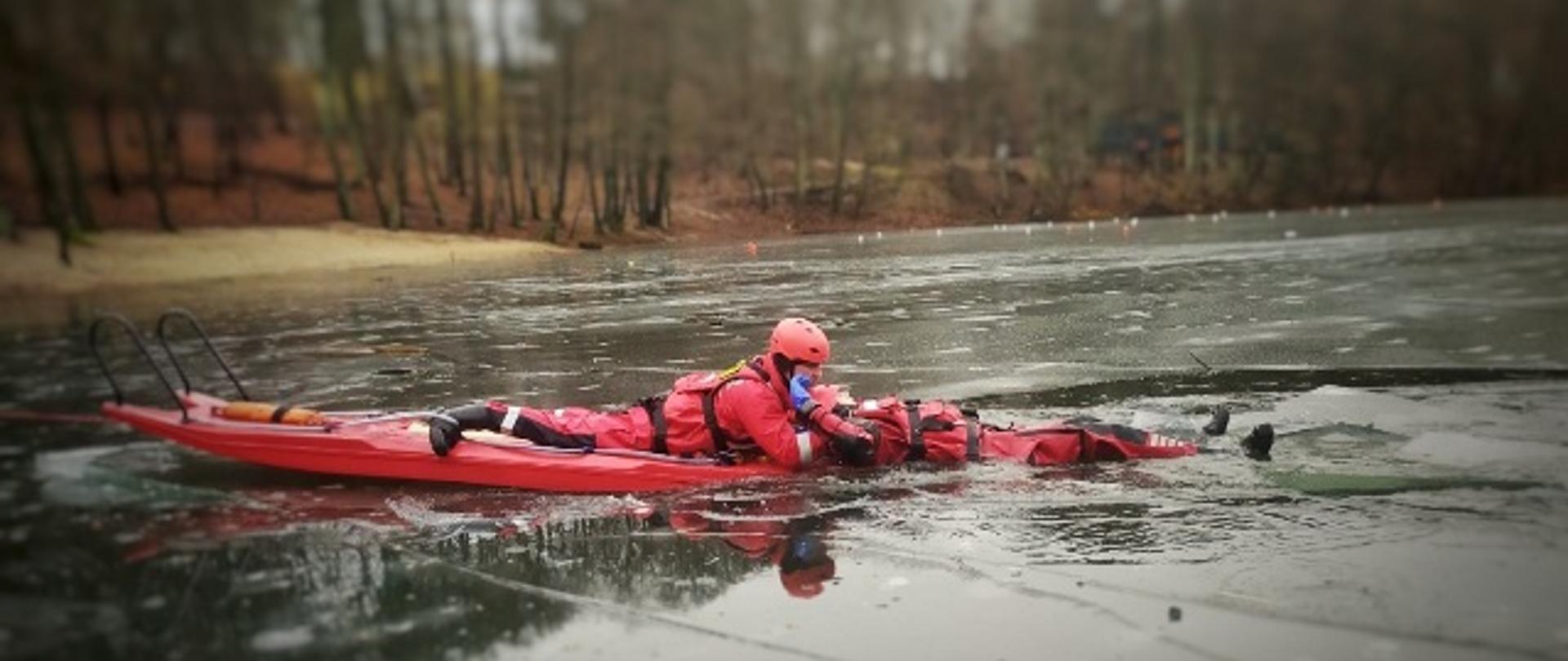 Strażak ewakuuje osobę pod którą załamał się lód przy użyciu deski lodowej.