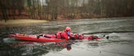 Strażak ewakuuje osobę pod którą załamał się lód przy użyciu deski lodowej.