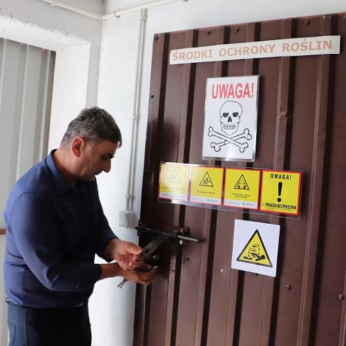 Rolnik otwiera drzwi z oznaczeniami o miejscu przechowywania środków chemicznych