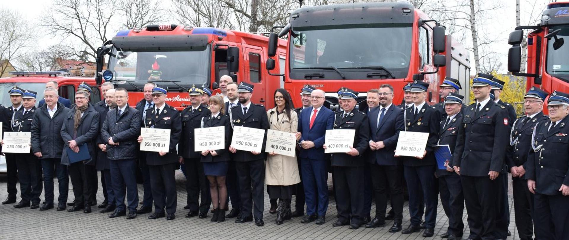 Obraz przedstawia przedstawicieli jednostek OSP, władze gmin i Komendantów Powiatowych pozujących do wspólnego zdjęcia z okazji wręczenia promes na zakup pojazdów pożarniczych