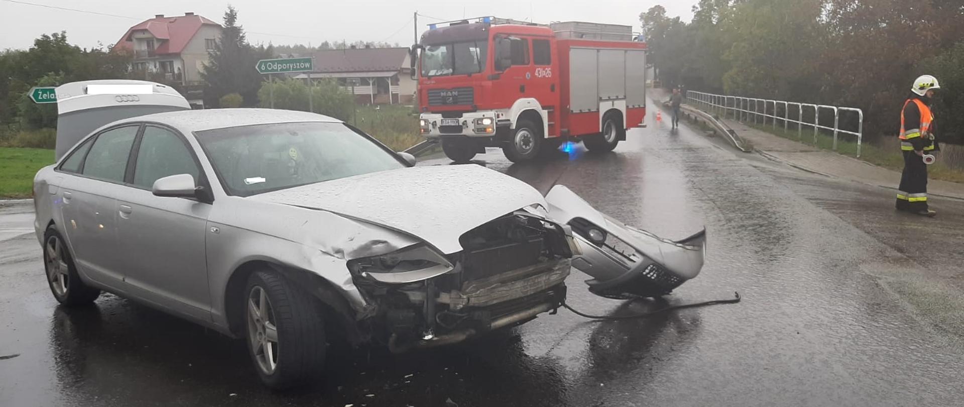 na zdjęciu przód pojazdu biorącego udział w kolizji, w oddali widać pojazdy ratownicze.
