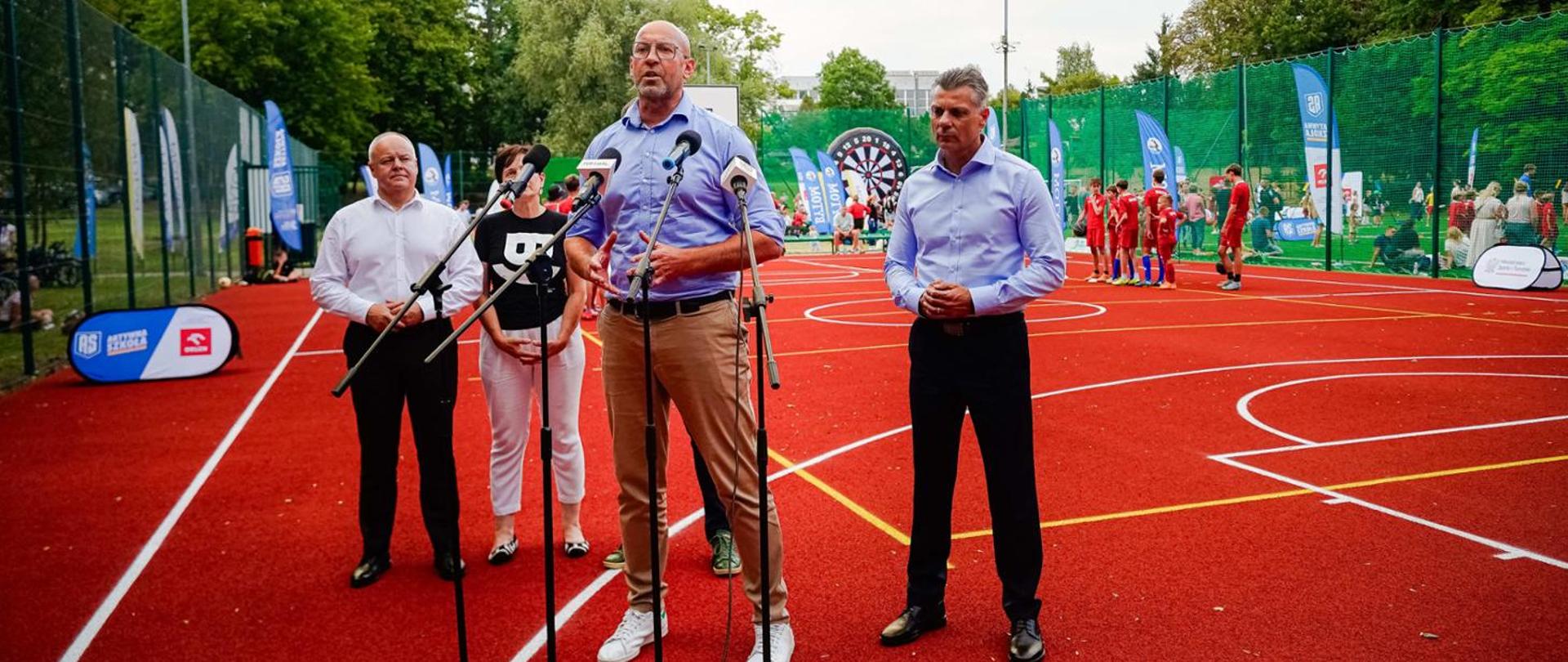 Press conference held at Orlik sport facility. Participants stand behind microphones. Minister of Sport and Tourism Jakub Rutnicki in the foreground, children in the background.