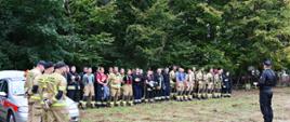 zbiórka strażaków przed rozpoczęciem ćwiczeń z boku srebrny samochód strażacy stoją na tle drzew