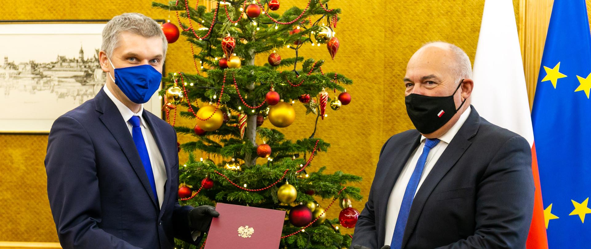 Minister finansów Tadeusz Kościński i wiceminister Piotr Nowak, który trzyma akt odwołania ze stanowiska, w tle choinka