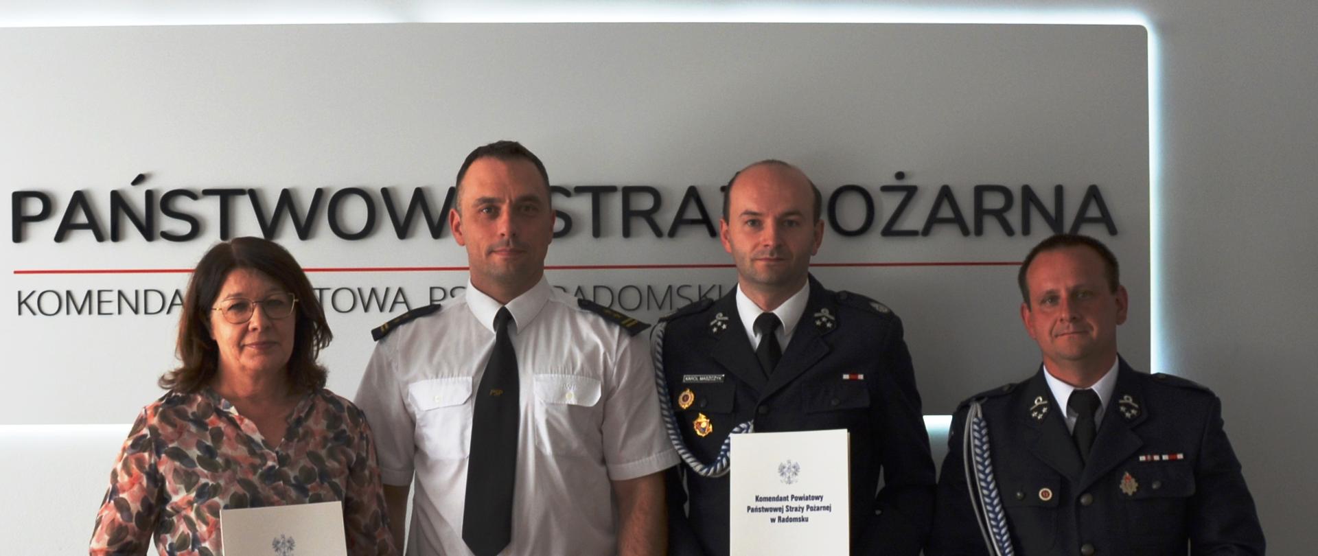 Trzech strażaków w umundurowaniu oraz kobieta w ubiorze cywilnym prezentują podpisane dokumenty.