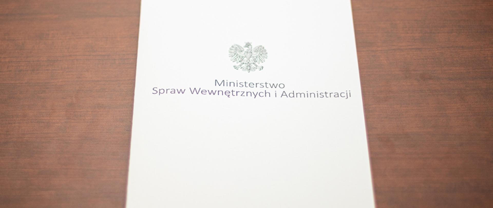Na zdjęciu widać leżącą teczkę z napisem "Ministerstwo Spraw Wewnętrznych i Administracji" i orłem z godła narodowego.