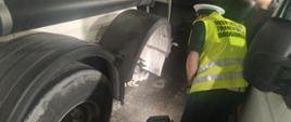 Umundurowany inspektor kujawsko-pomorskiej Inspekcji Transportu Drogowego stoi obok naczepy bez koła, która jest właśnie naprawiana przez mobilny serwis.