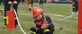Kolejne zdjęcie z zawodów Młodzieżowych drużyn pożarniczych na którym widać dwójkę zawodników używających hydronetki (ręcznej pompy z wężem z którego leci woda i wypełnia zbiornik). W tle widać sędziów z PSP.